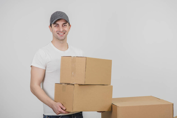Delivery man standing, holding two carton boxes, looking at the camera, smiling. - Photo, image
