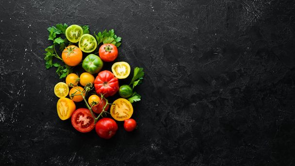Vegetables. Fresh colored tomatoes On a black stone background. Top view. Free space for your text. - Fotó, kép