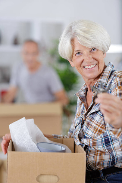 portret van lachende oudere vrouw die dozen uitpakt - Foto, afbeelding