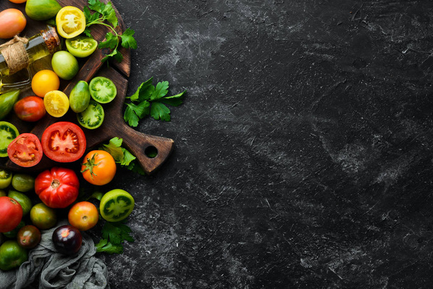 Vegetables. Fresh colored tomatoes On a black stone background. Top view. Free space for your text. - Foto, Imagem