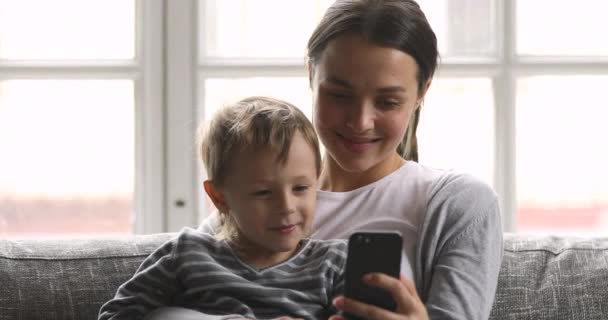 Happy mom teaching kid son laughing using looking at phone - Materiał filmowy, wideo