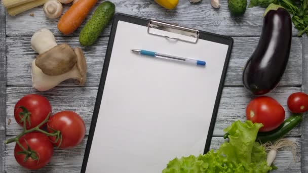 Pen rolling on clipboard on kitchen table with vegetables - Footage, Video