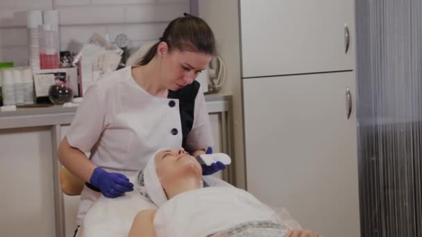 Professzionális kozmetikus ultrahangos arctisztítást végez középkorú nők számára. - Felvétel, videó