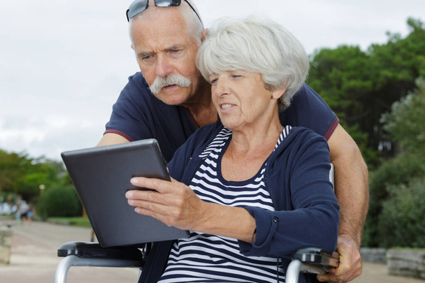 senior couple using a tablet outdoors woman in wheelchair - Zdjęcie, obraz