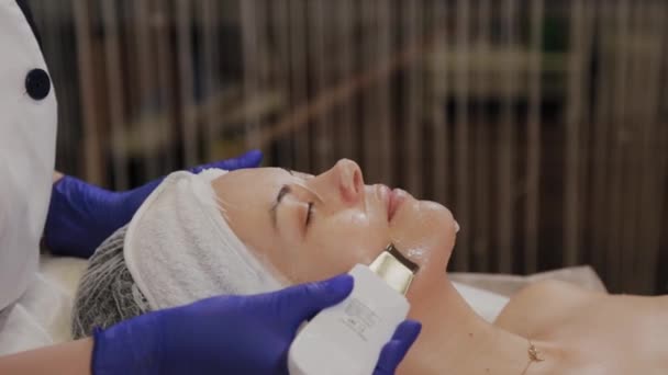 Profesyonel güzellik uzmanı orta yaşlı bir kadın için ultrasonik yüz temizliği yapıyor.. - Video, Çekim