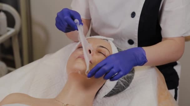 Egy profi kozmetikus eltávolítja az átlátszó szövet anti-aging maszk egy nő arcát. - Felvétel, videó