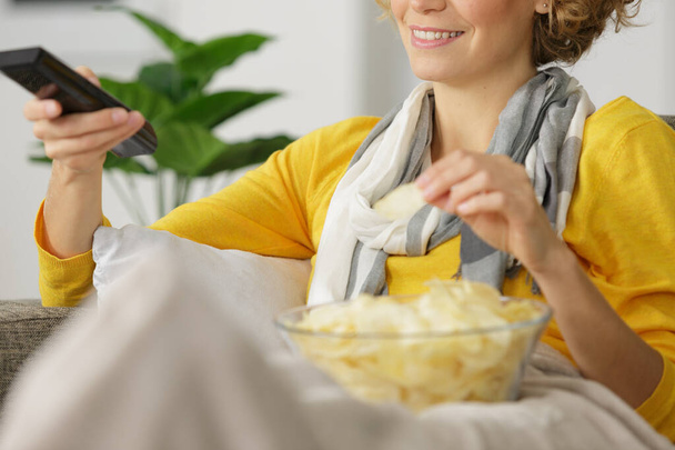 woman with bowl by chips and tv remote control - 写真・画像