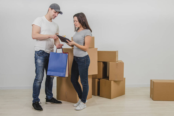 Handsome courier delivered presents in colorful bags for young woman on the occasion of her moving into new apartment. Woman is really happy and is signing the declaration. - 写真・画像