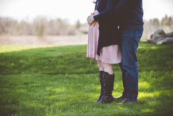 Closeup shot of a pregnant couple standing on a grassy field with a blurred background - Photo, Image
