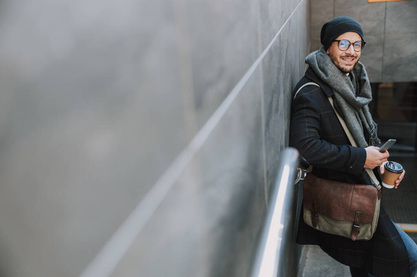 Caucasian guy in warm clothes drinking coffee on stairs - Foto, Bild