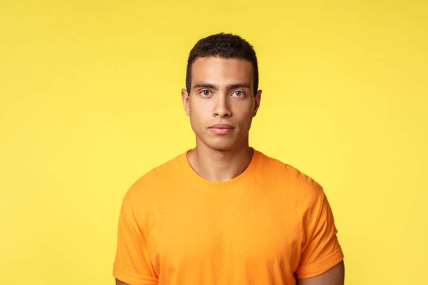 Motivation, lifestyle and sport concept. Serious-looking determined handsome young masculine man in t-shirt look camera focused with no facial expression, listening teacher, yellow background - Photo, Image