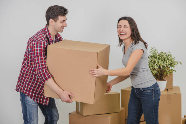 Couple in a new flat. Young man is totaly exhausted. He can not hold heavy box anymore, he almost dropped it, but woman helped him. - Foto, Imagen