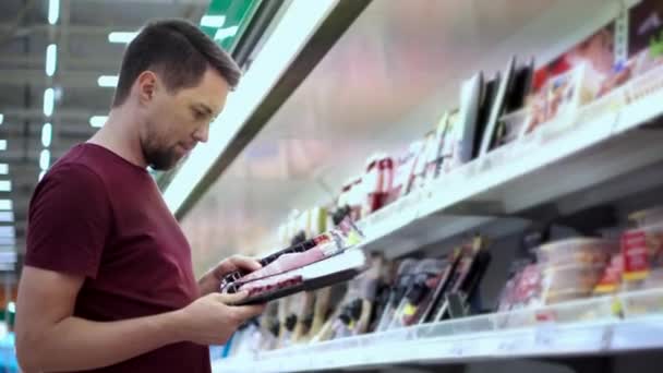 Zákazník muž srovnává dvě balení klobás v supermarketu - Záběry, video