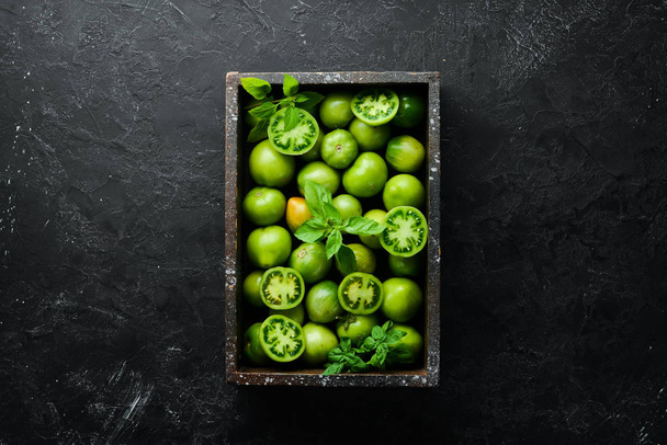 Siyah taş zemin üzerinde ahşap kutuda yeşil domatesler. Yeşiller. Üst Manzara. Metnin için boş yer. - Fotoğraf, Görsel