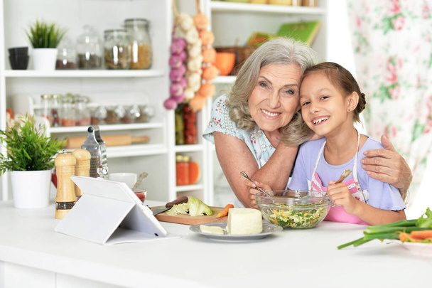 Cute little girl with her grandmother cooking together at kitchen table  - Фото, зображення
