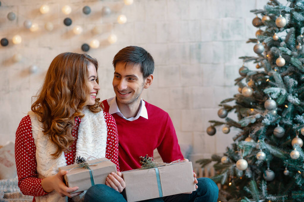 Happy young couple with Christmas presents on a decorated tree background - Zdjęcie, obraz