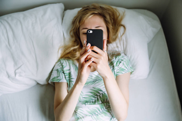 Vrouw leest een bericht in haar telefoon liggend op het bed - Foto, afbeelding