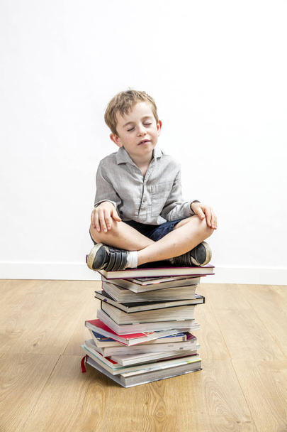 smiling serene boy meditating seated on top of mindfulness books - Fotó, kép