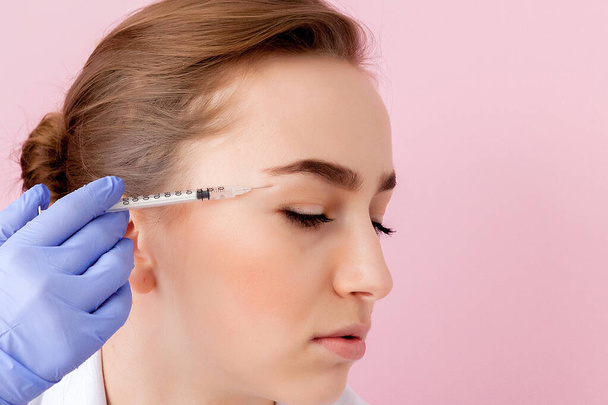 The doctor cosmetologist makes the Botulinotoxin injection procedure for tightening and smoothing wrinkles on the face skin of a beautiful, young woman in a beauty salon.Cosmetology skin care - Photo, Image