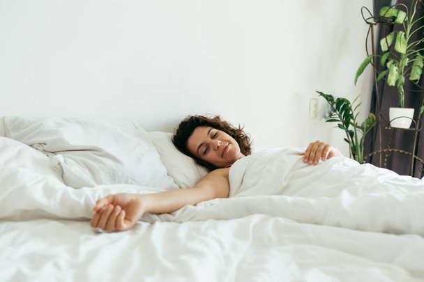 jovem mulher bonita na cama com lençóis brancos luz brilhante
 - Foto, Imagem
