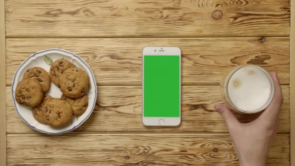 Περικοπή πρόσωπο πίνοντας καφέ και τρώγοντας cookies κοντά smartphone - Πλάνα, βίντεο