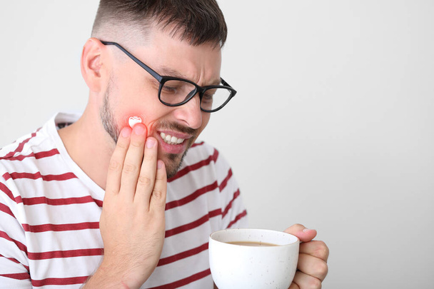 Homem com dentes sensíveis e café quente no fundo claro
 - Foto, Imagem