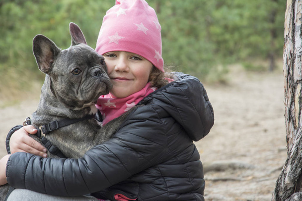 En el bosque de otoño, una niña sostiene un bulldog francés en él
 - Foto, imagen