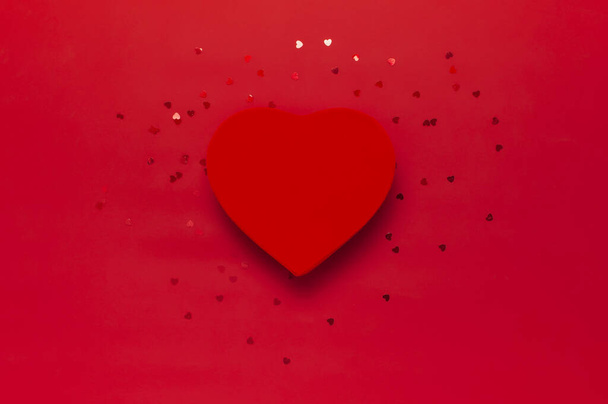 Red gift box in the shape of heart and confetti on red background top view Flat lay. Creative composition for Valentine's Day, love concept, birthday present, mother day, holiday background - 写真・画像