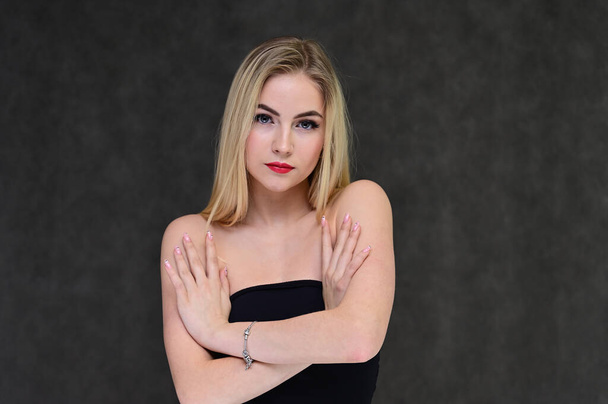 The concept of fashionable glamor, cosmetics and beauty with a pretty girl. Portrait of a fashionable beautiful blonde model with long hair, great makeup, on a gray background. - Foto, afbeelding