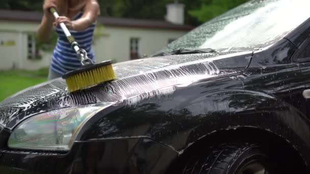 Female worker washing car automobile hood with long brush and shampoo foam - Footage, Video