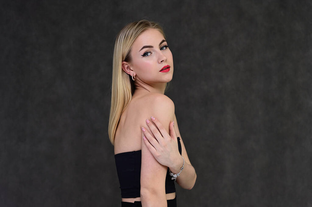 The concept of fashionable glamor, cosmetics and beauty with a pretty girl. Portrait of a fashionable beautiful blonde model with long hair, great makeup, on a gray background. - Foto, Imagen