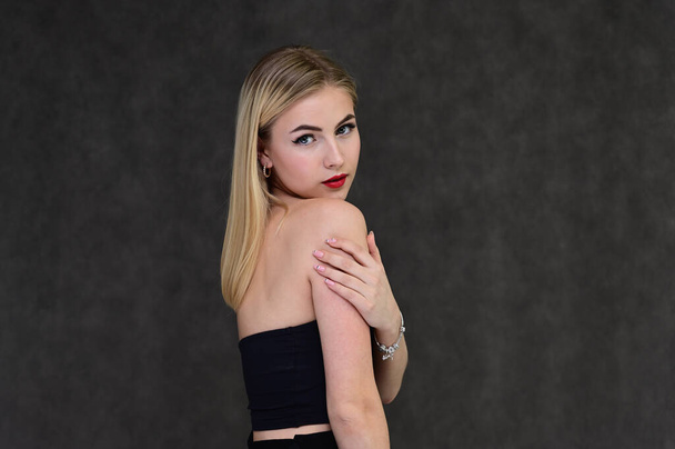The concept of fashionable glamor, cosmetics and beauty with a pretty girl. Portrait of a fashionable beautiful blonde model with long hair, great makeup, on a gray background. - Zdjęcie, obraz