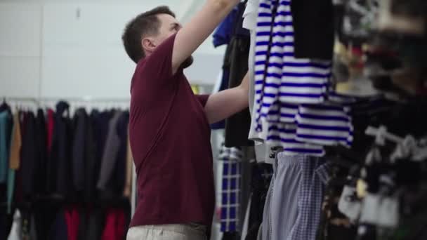 バイヤーマンは、衣料品店の貿易分野でTシャツを選択しています - 映像、動画