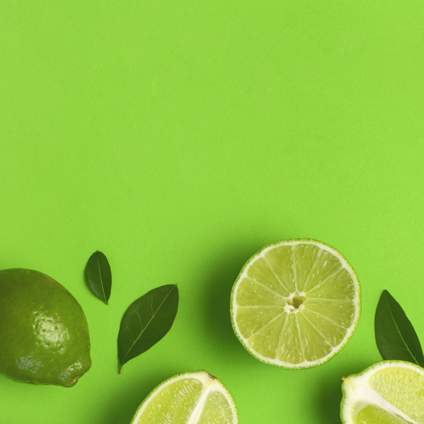 Fresh juicy lime and green leaves on bright green background. Top view flat lay copy space. Creative food background, tropical fruit, vitamin C, citrus. Composition with whole and slices of lime - Photo, Image