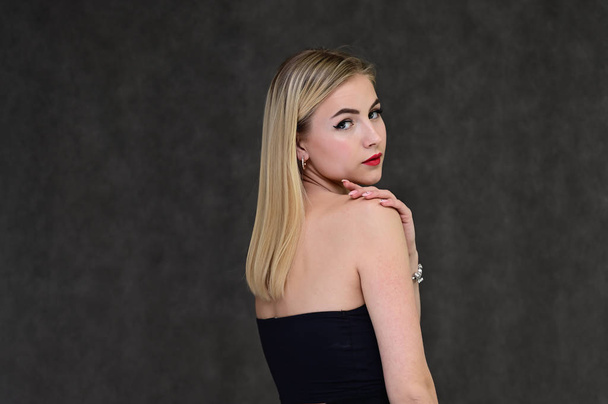 The concept of fashionable glamor, cosmetics and beauty with a pretty girl. Portrait of a fashionable beautiful blonde model with long hair, great makeup, on a gray background. - 写真・画像
