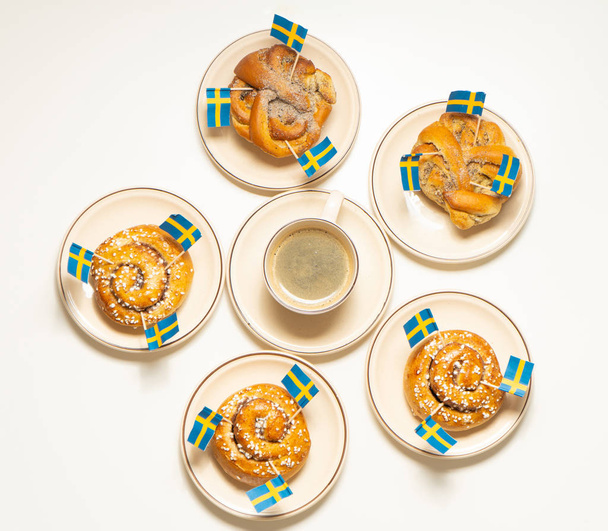 İsveç tarçınlı çörekler (kanelbullar) ve beyaz ahşap masada kahve. İsveç bayrakları. Kahve molası (fika) kavramı. Üst görünüm.  - Fotoğraf, Görsel