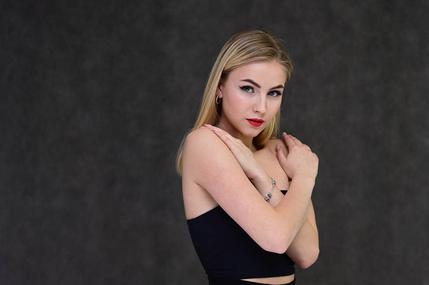 The concept of fashionable glamor, cosmetics and beauty with a pretty girl. Portrait of a fashionable beautiful blonde model with long hair, great makeup, on a gray background. - 写真・画像