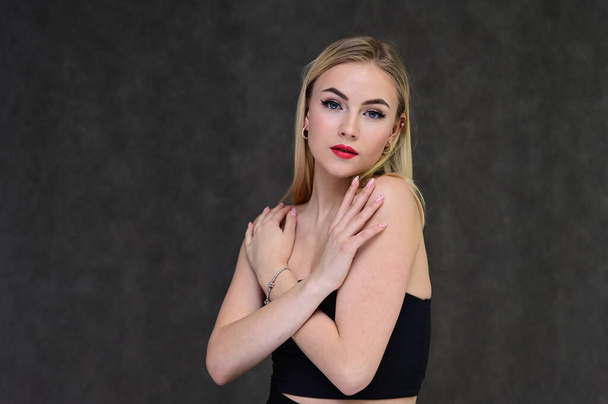 The concept of fashionable glamor, cosmetics and beauty with a pretty girl. Portrait of a fashionable beautiful blonde model with long hair, great makeup, on a gray background. - Foto, imagen