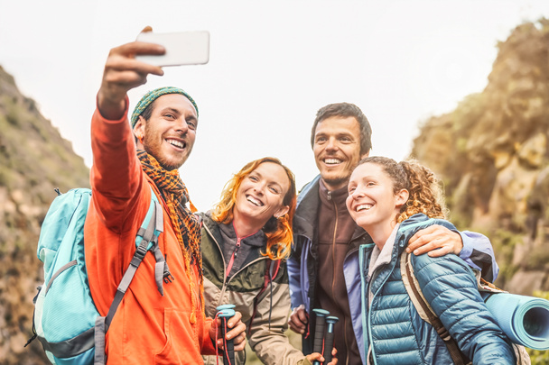 Happy friends taking photo selfie with mobile smartphone camera on mountains - Group young people trekking and having fun with new technology trends - Sport, hiking, Tech and social media concept - 写真・画像
