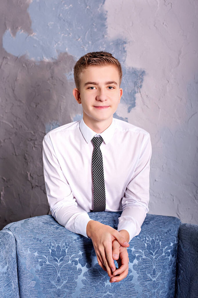 close portrait of a teenager in a shirt with a tie in the studio near an armchair - Foto, Bild