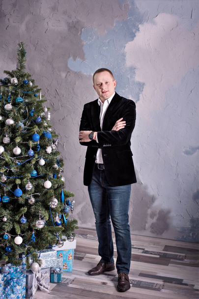 An attractive man in lifestyle clothing is standing near the Christmas tree. - Foto, Bild