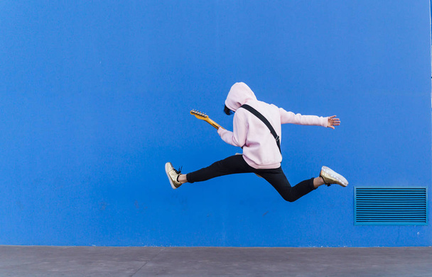 young man jumping with electric guitar on blue background - Photo, image