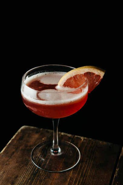 Pink cocktail garnished with a slice of blood orange on dark bac - Fotó, kép