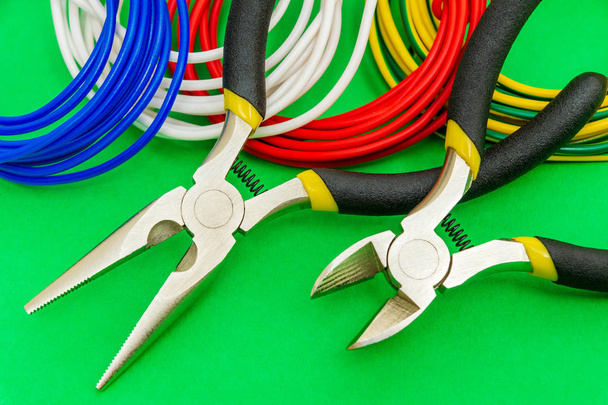 Плоскогубцы инструмент и провода для электрика крупным планом на зеленом фоне
 - Фото, изображение