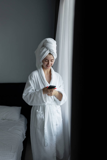 a woman in a bathrobe is standing by the window reading a message. - Fotoğraf, Görsel