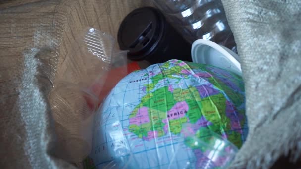 The pollution of the planet with plastic waste. Ecology and zero waste concept. World globe in the trash bin with waste plastic garbage - Materiał filmowy, wideo