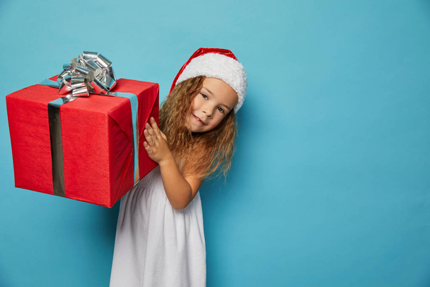  Girl in Santa red hat holding Christmas gift - Foto, Imagen