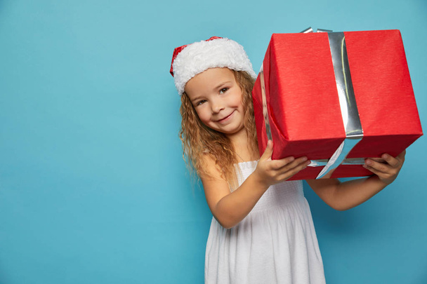  Girl in Santa red hat holding Christmas gift - Foto, imagen