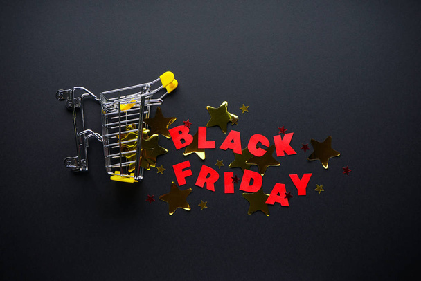 Black friday concept. Black Friday sale red letters. Yellow confetti and a basket on a black background. Flat lay - Fotoğraf, Görsel