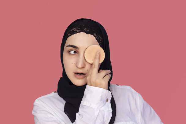 Leuke twintiger jaren vrouw die poeder met spons op haar gezicht aanbrengt. Mooie Perzische vrouw in hijab doet make-up - Foto, afbeelding